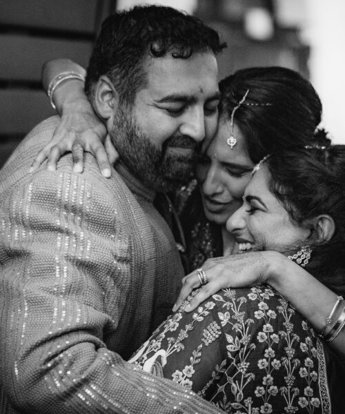 Three people in traditional attire share a joyful, tearful group hug at a celebration.