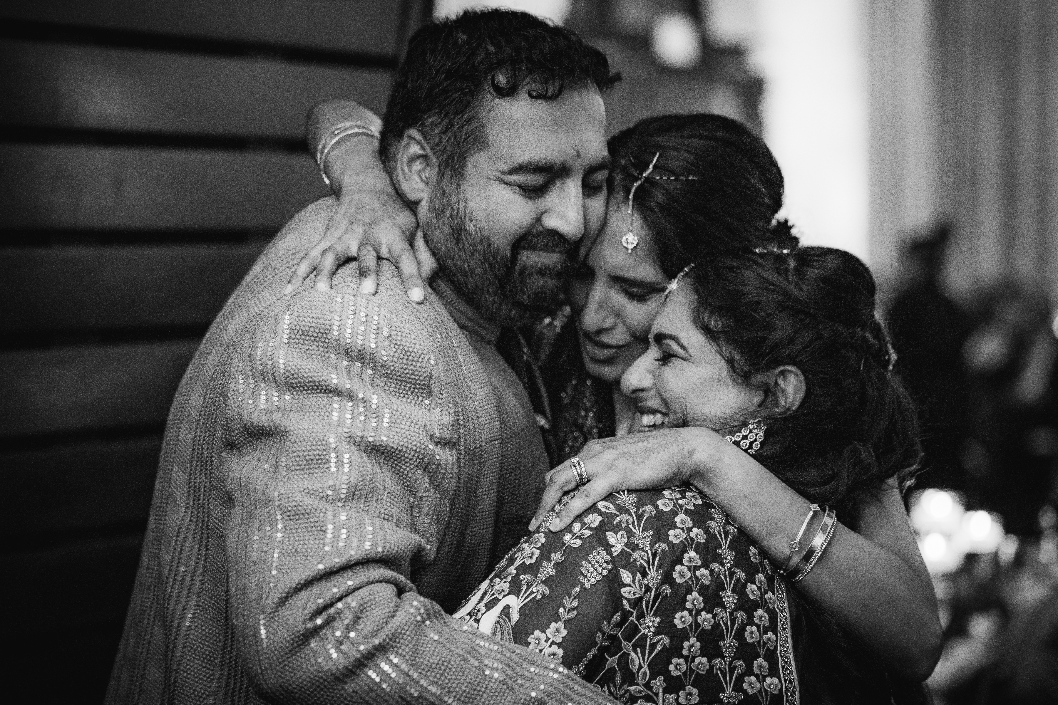 Three people in traditional attire share a joyful, tearful group hug at a celebration.