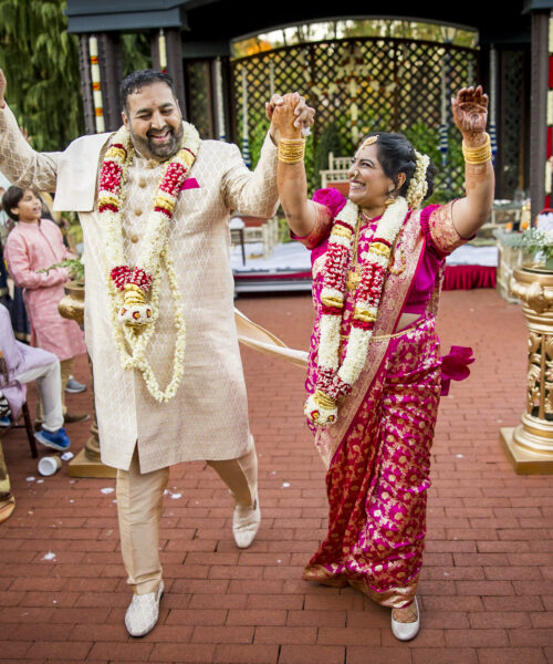 A joyful couple in traditional attire celebrates at an outdoor wedding ceremony as guests cheer around them.