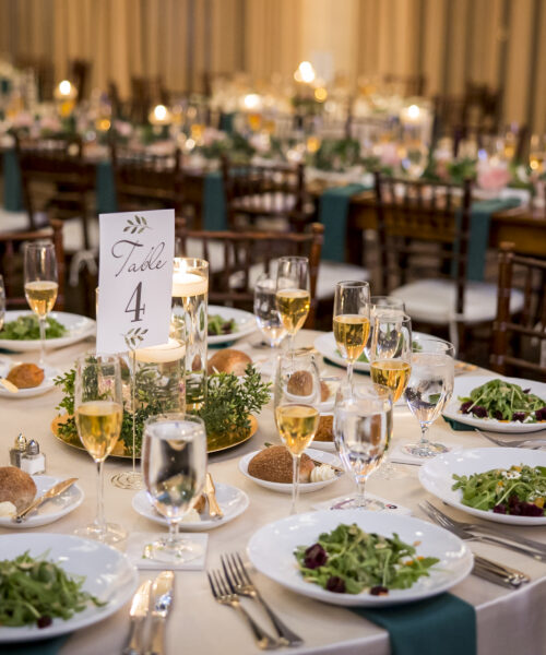 Elegant banquet table set with salads, bread, wine glasses, and a Table 4 sign at a formal event.