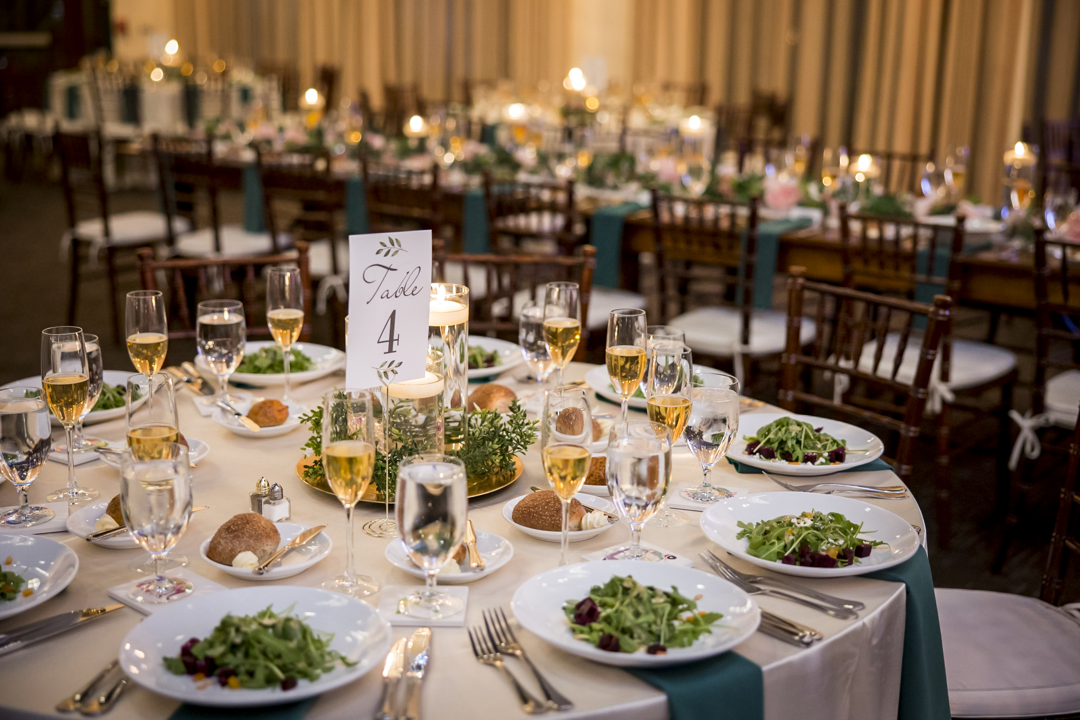 Elegant banquet table set with salads, bread, wine glasses, and a Table 4 sign at a formal event.