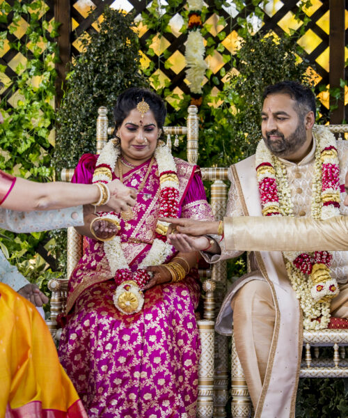 Indian wedding ceremony with bride and groom in traditional attire, joined by two elders for a ritual.