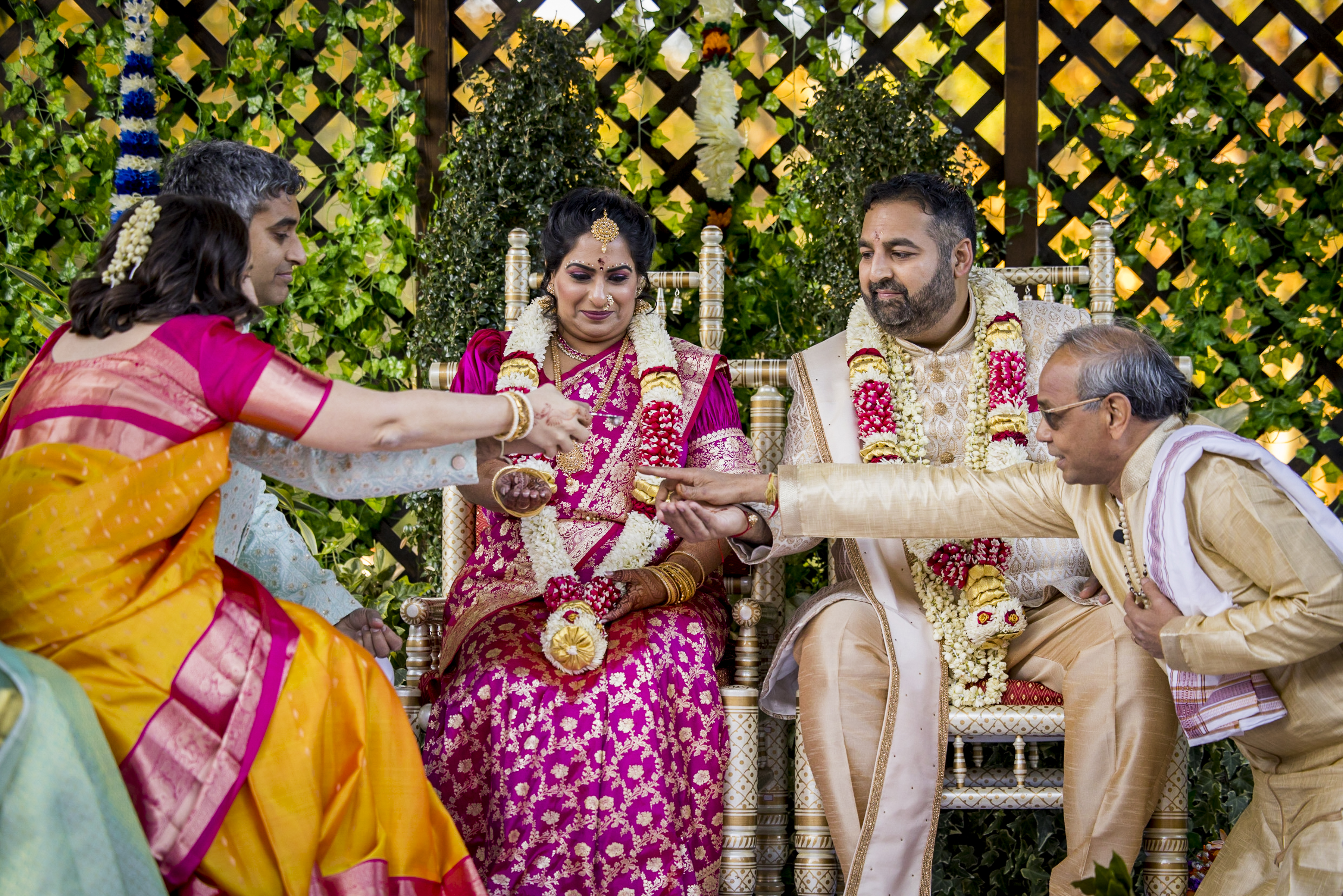 Indian wedding ceremony with bride and groom in traditional attire, joined by two elders for a ritual.