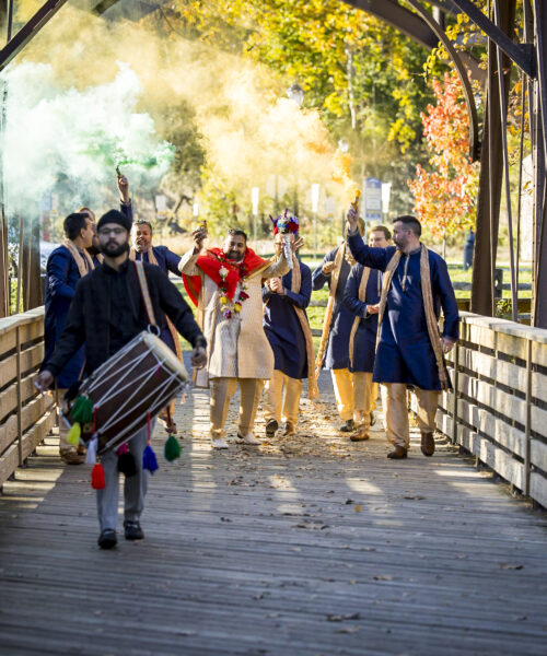 A group of people in traditional attire celebrate with colored smoke on a wooden bridge in autumn.