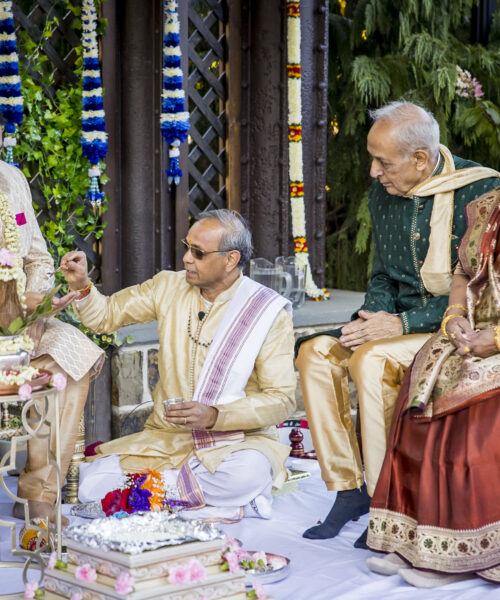 A Hindu wedding ceremony with four adults in traditional attire performing rituals outdoors.