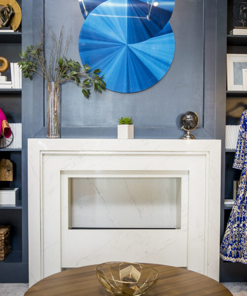 A modern living room with a fireplace, colorful dresses on display, and stylish shelves with decor.