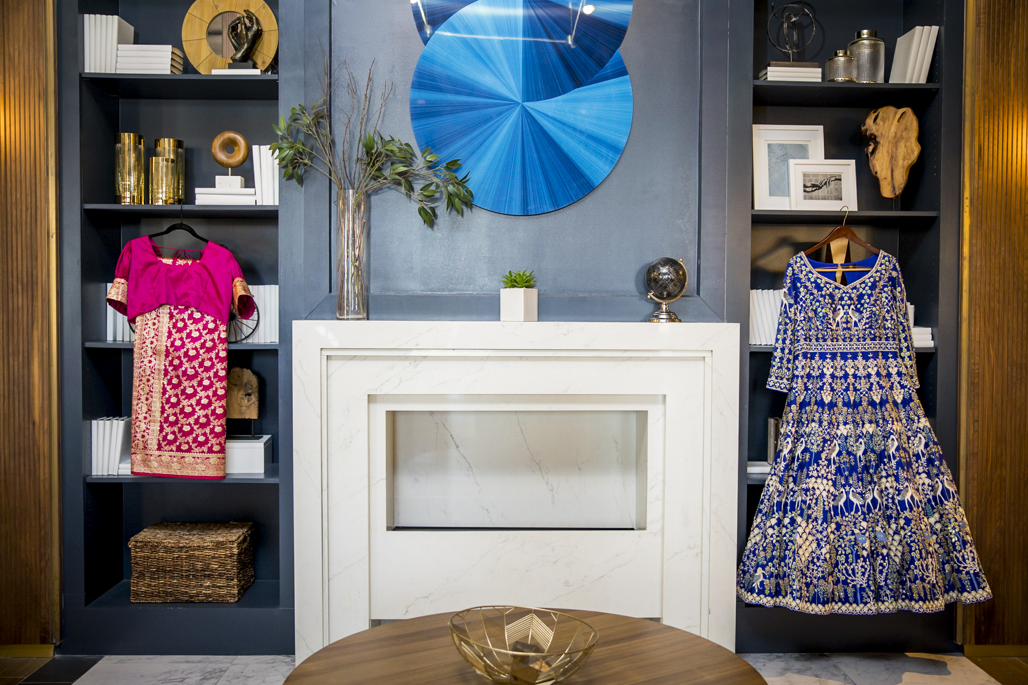A modern living room with a fireplace, colorful dresses on display, and stylish shelves with decor.