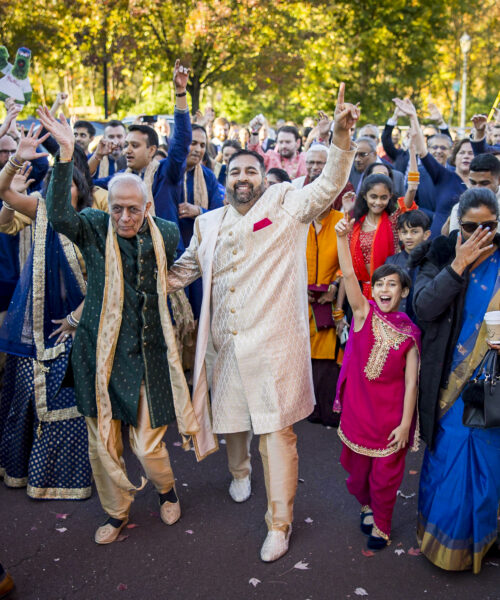 A joyful group in colorful traditional clothing celebrates outdoors, smiling and raising their hands.