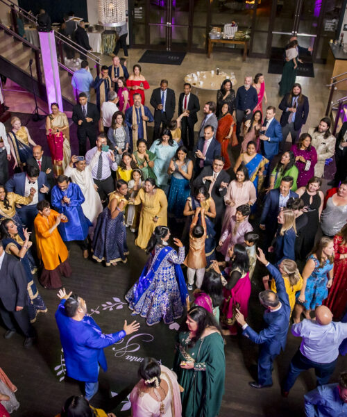 A large group of people in colorful attire dance and celebrate in a decorated indoor venue.