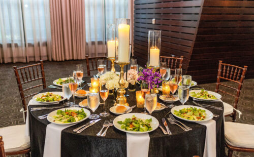 A round table set for six with salads, rolls, drinks, and candles as the centerpiece in an elegant room.