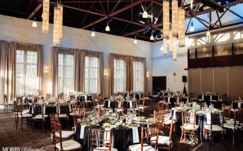 Elegant banquet hall set for an event with round tables, black linens, and hanging lights.